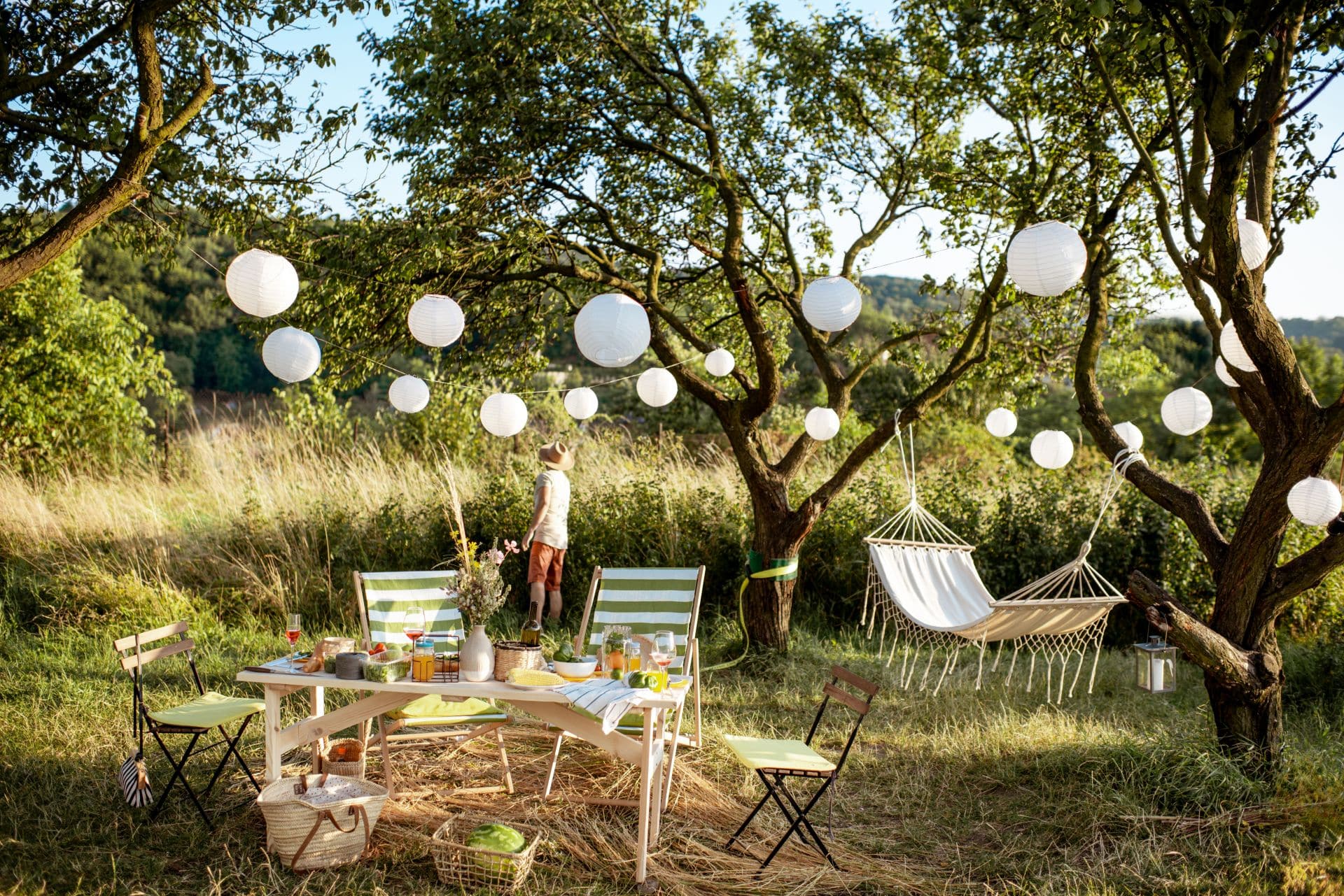 Ein stilvoller Essbereich im Garten mit Hängematte, dekoriert mit Papierlaternen zwischen den Bäumen, perfekter Ort zum Entspannen unter Pavillons.