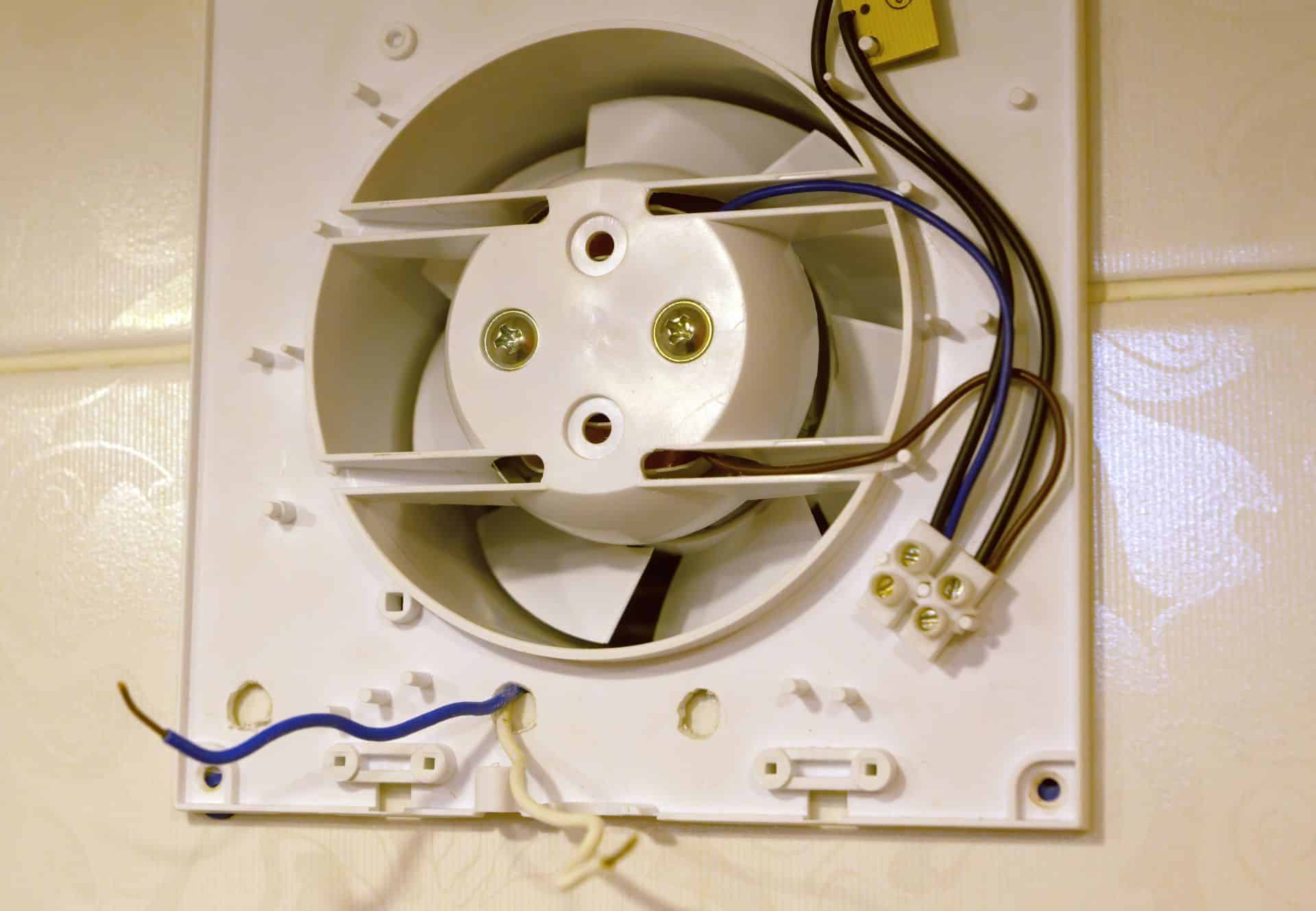 Weisser Wandluefter mit sichtbarem Luefterrad und elektrischer Verdrahtung vor der Montage im Badezimmer