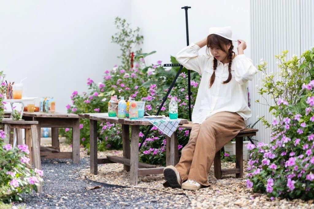 Junge Frau sitzt entspannt im blühenden Garten auf rustikaler Bank neben einem Kiesweg – kreative Gartengestaltung mit Farben und Natur.