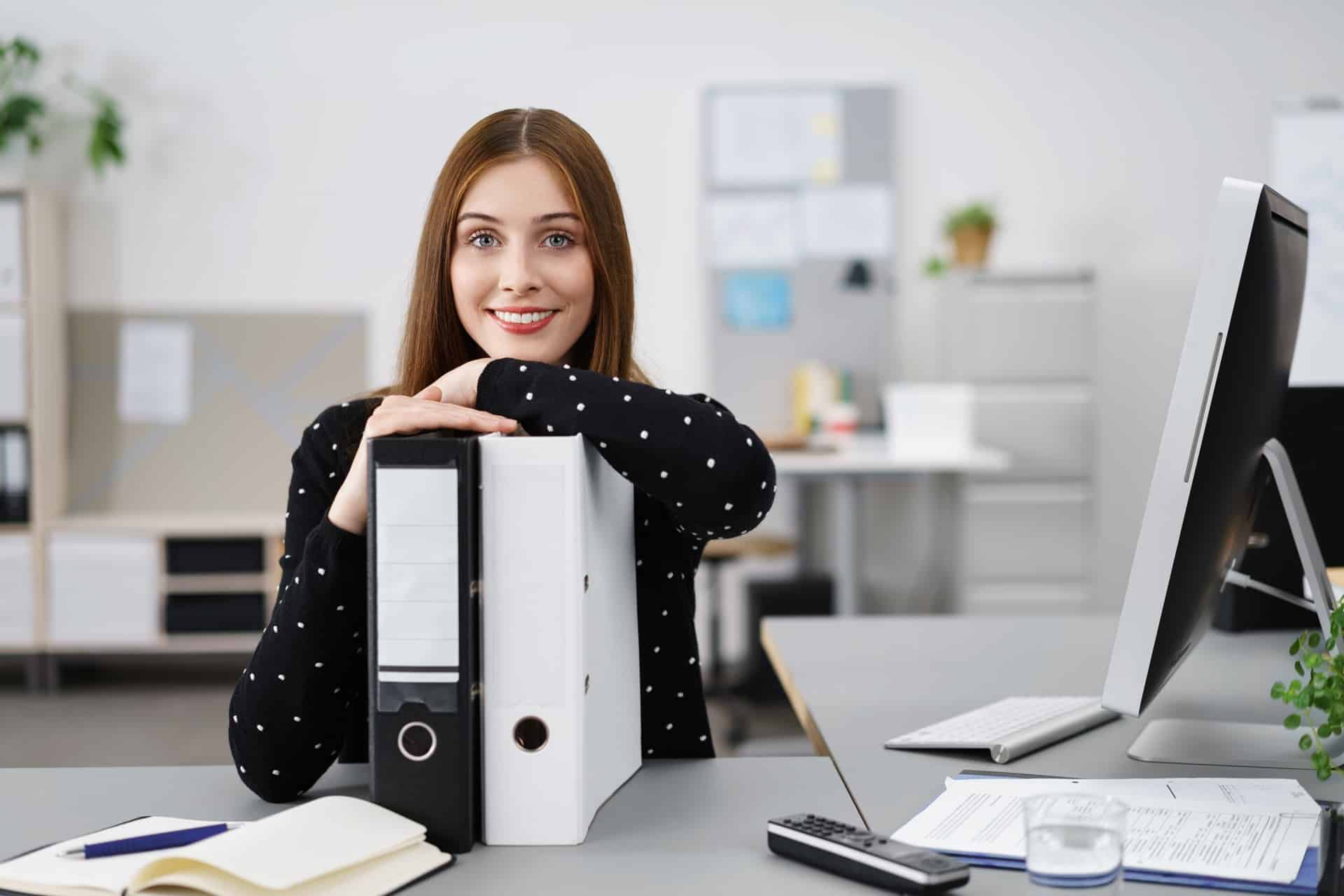 Freundliche Mitarbeiterin mit Aktenordnern im Büro | Lohnabrechnung outsourcen